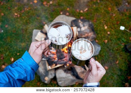 Wanderlust And Travel Concept. Metal Cups With Hot Chocolate And Marshmallows. Fire On Background. A