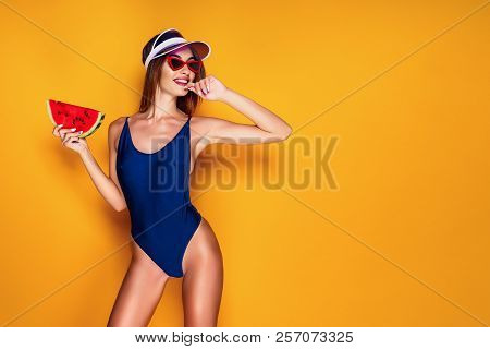 Beautiful Young Lady In Swimwear Biting Finger And Holding Piece Of Fresh Watermelon While Standing 