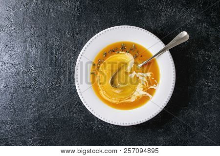 Plate Of Vegetarian Pumpkin Carrot Soup Decorated By Herbs And Cream, With Spoon Inside Over Black T