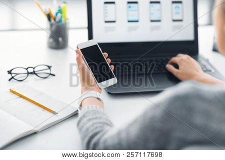 app design, technology and business concept - web designer or developer with smartphone and laptop computer working on user interface at office