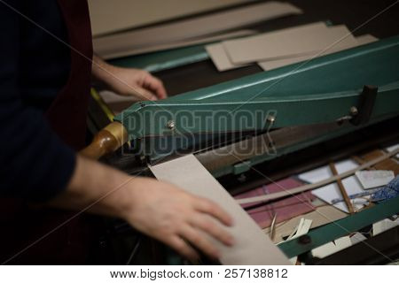 Man Cutting Paper And Card On A Large Guillotine On A Work Table In A Book Binders Workshop In A Clo