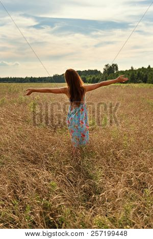 Young Woman Girl Standing With Her Back With Open Arms To The Sunset On A Wheat Field In The Country