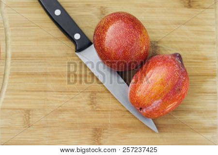 A Pair Of Amigo Pluots Besides A Knife On A Wood Cutting Board