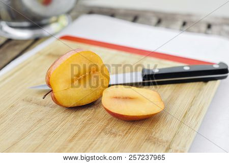 An Amigo Pluot Fruit Sliced Open With A Knife On A Cutting Board