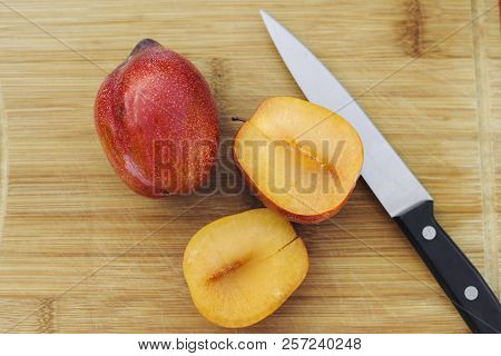 One Full Pluot Alongside A Cut Open Amigo Pluot And A Knife