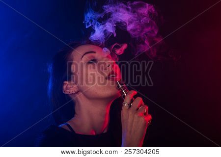 Young Woman In Neon Light And Smoke Of E-cigarettes Or Vape On Dark Background