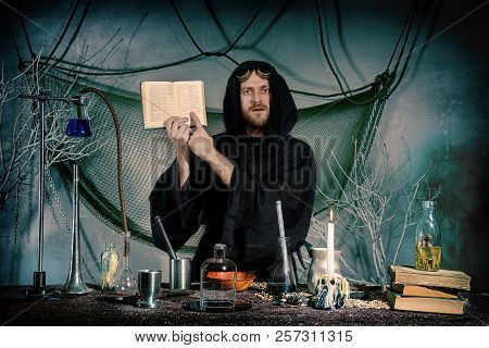 Portrait Of A Crazy Alchemist. The Medieval Scientist Indicates The Text In The Recipe Book. Hallowe