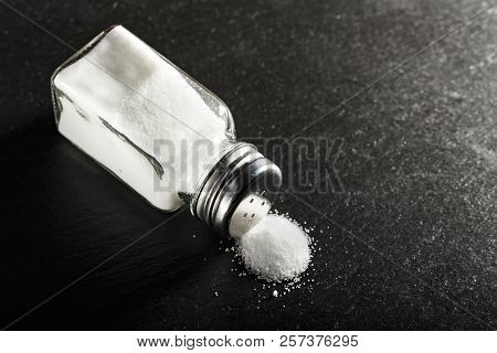 The Salt Of Fine Grinding Scattered From Saltcellar On A Black Table. Place For Text