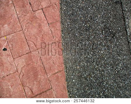 A Section Of Red Stonework And Black And Gray Mottled Macadam.