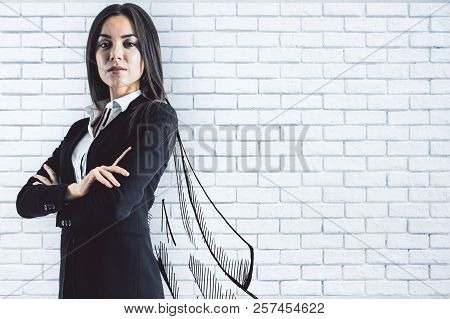 Portrait Of Attractive Young European Businesswoman With Drawn Cape On Brick Wall Background. Leader
