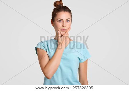 Thoughtful Puzzled Woman With Hesitant Expression, Holds Chin, Dressed In Casual Clothes, Ponders On