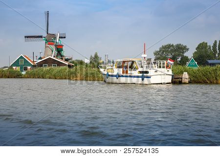 Traditional, Authentic Dutch Windmill And Boat At The River Zaam In Zaanse Schans Village.