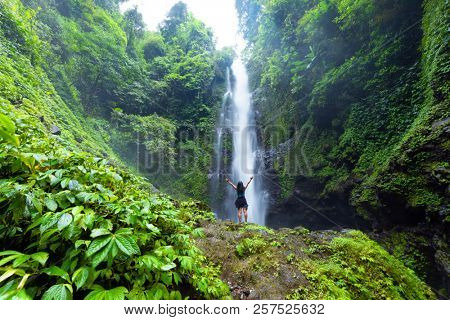 Woman enjoying and relaxing in front of the Laangan waterfall in the Munduk forest, Bali island, Indonesia