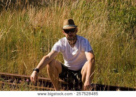 A Lonely Man In A Strawy Hat Sitting On A Rails.