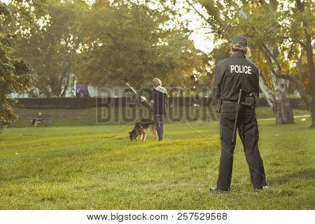 Policeman In Uniform Checking Lady With German Shepherd In City Park