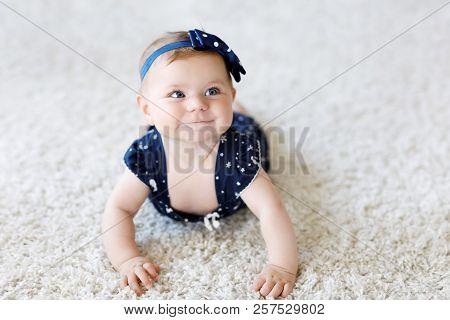 Cute Adorable Baby Girl In Blue Clothes And Headband. Little Child Looking At The Camera And Crawlin