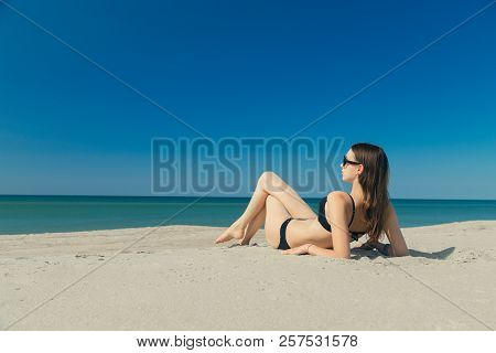 Beautiful Young Woman In Swimsuit At Sand Sea Beach Lying Under Sun Rays Tanning, Toned Image