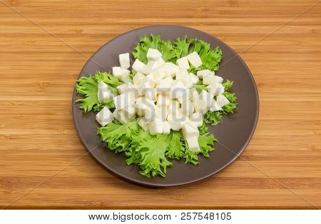 Brown Dish With Mozzarella Cheese Sliced Into Small Cubes On Lettuce Leaves On A Bamboo Wooden Surfa