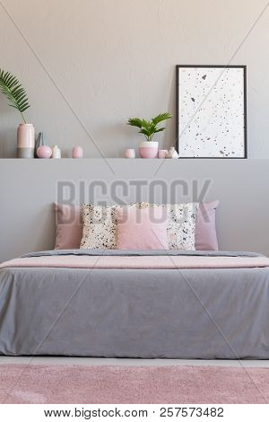 Pink Carpet In Front Of Grey Bed With Cushions In Bedroom Interior With Plants And Poster. Real Phot