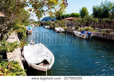 Clean River In A Summer Warm Place With A Lot Of Greenery And Sun, White Boat In The Front