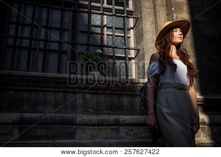 Outdoor Portrait Of Young Tourist Woman Walking On Old City Street. Traveler Girl Looking At Ancient