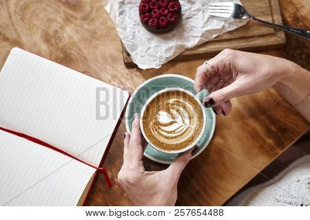Cup Of Coffee Latte On Wooden Table Or Background In Woman Hands From Above. Having Lunch In Cafe. O