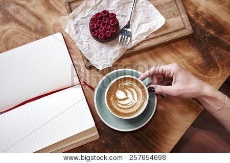 Cup Of Coffee Latte On Wooden Table Or Background In Woman Hands From Above. Having Lunch In Cafe. O