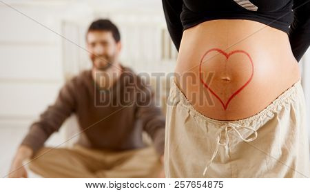 Close-up of pregnant belly with drawn heart shape.
