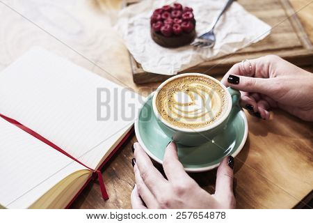 Cup Of Coffee Latte On Wooden Table Or Background In Woman Hands From Above. Having Lunch In Cafe. O