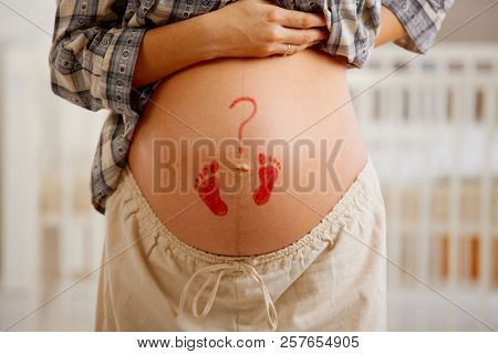 Close-up of pregnant belly with little drawn footprints and question mark.