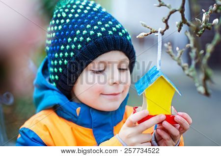 Little Kid Boy Feeding Birds In Winter. Child Hanging Colorful Selfmade Bird House On Tree On Frosty