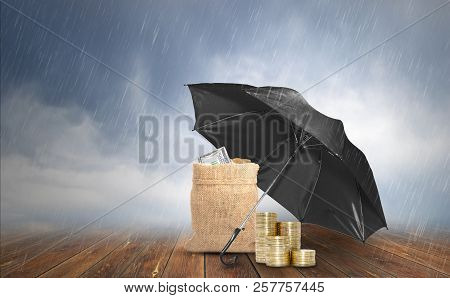 Protection Concept, Black Umbrella Protect Stack Of Coins And Sack Bag With Dollar Bills On Wooden B