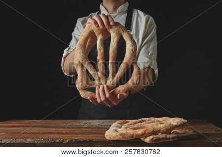 Delicious freshly baked fougas bread in the hands of a man on a black background