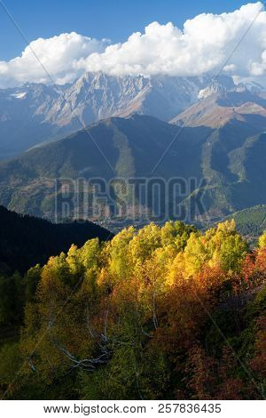 Autumn in Zemo Svaneti, Georgia. Ushba peak in clouds. View from Mount Mkheer. Landscape with birch forest on the hillside. Main Caucasian ridge