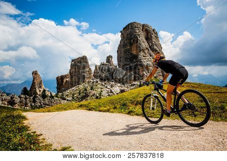 Tourist cycling in Cortina d'Ampezzo, stunning rocky mountains on the background. Woman riding MTB enduro flow trail. South Tyrol province of Italy, Dolomites.
