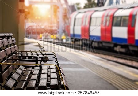 Empty Wooden Bench On The Platform And Approaching Overground Train In The Background, London, Uk