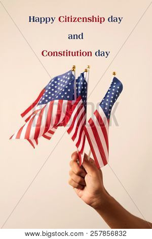 closeup of a man weaving some flags of the United States and the text happy citizenship day and constitution day against an off-white background