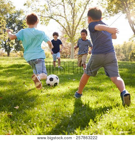 Four schoolboys playing football in the park, square format