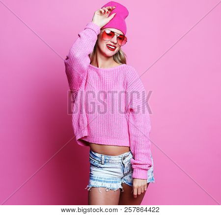 Stylish fashion portrait of trendy casual young woman in pink pulover and hat, posing over pink background.
