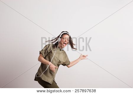Young Woman With Headphones, Listening To Music, Singing And Pretending To Play Guitar.