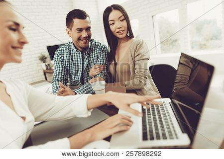 Young Man And Woman With Smiling Realtor In Office. Blueprint On Wooden Desk. Real Estate Concepts. 