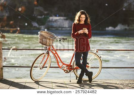 Theme Tourism On Bicycle And Modern Technology. Beautiful Young Caucasian Woman Stands Near Red Retr