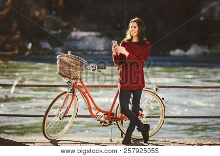 Theme Tourism On Bicycle And Modern Technology. Beautiful Young Caucasian Woman Stands Near Red Retr