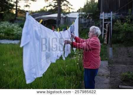An elderly woman hangs washed clothes in the yard of his village house.