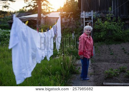 Elderly woman hangs washed clothes in the yard of his village house.
