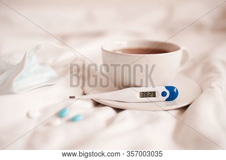 лекарства и градусник рядом с чашкой чая