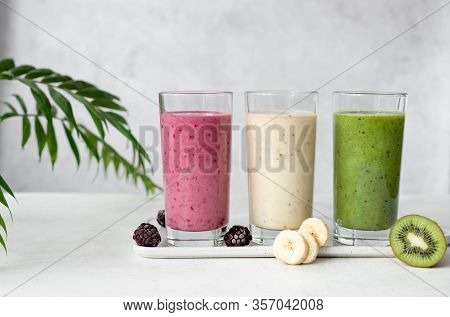 Different Types Of Smoothies On A Gray Background With Green Leaves. Black Berry, Banana, Kiwi And S