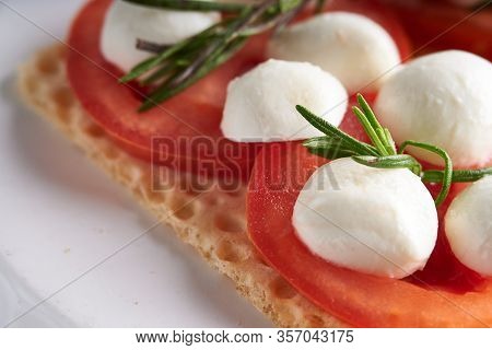 Toasts With Mozzarella, Tomatoes And Rosemary In A White Plate