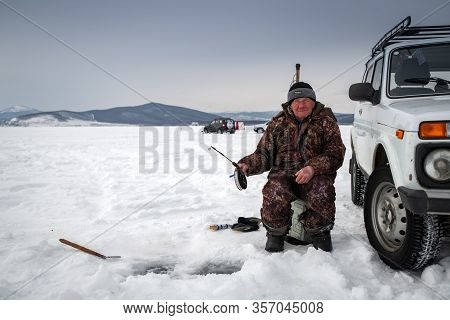 Baikal Lake, Siberia, Russia - March 05, 2020 : Winter Ice Fishing. A Fisherman Is Fishing On Spinin
