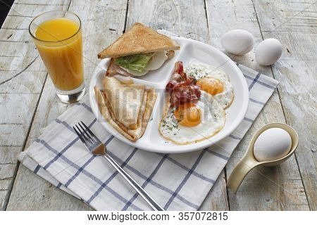 Breakfast Of Scrambled Eggs With Bacon, Pancakes, Sandwich And Orange Juice. On A Wooden Table